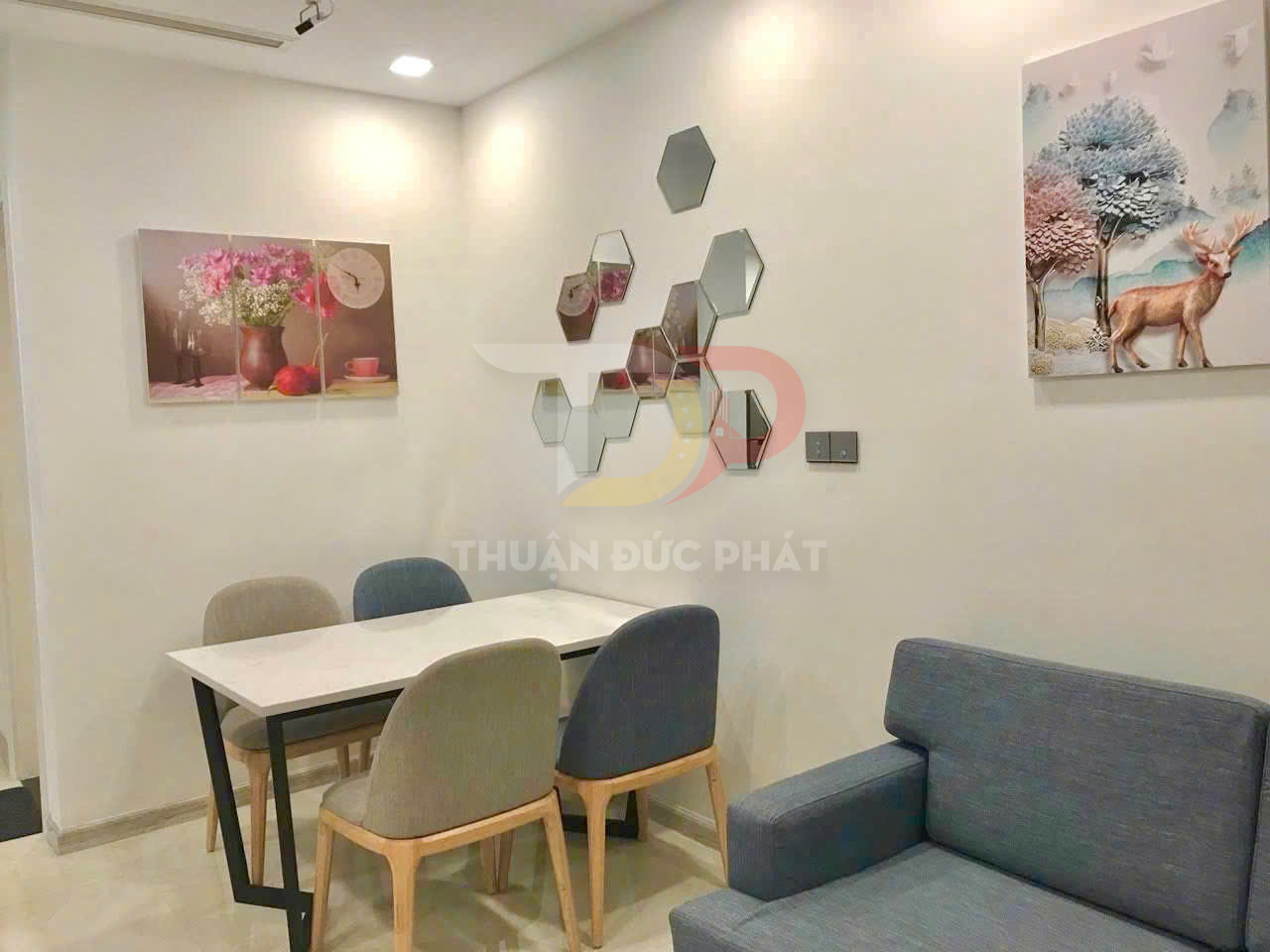 Bộ bàn ăn 4 ghế bọc nệm hiện đại đặt cạnh sofa và tranh treo tường trong phòng khách nhỏ