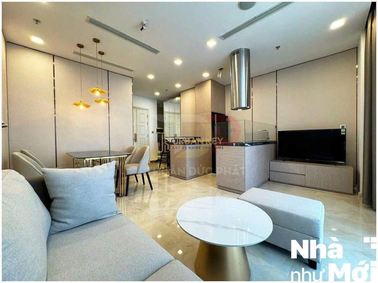 Phòng khách căn hộ hiện đại với sofa xám, bàn trà tròn, bếp mở và bàn ăn sang trọng ánh đèn vàng
