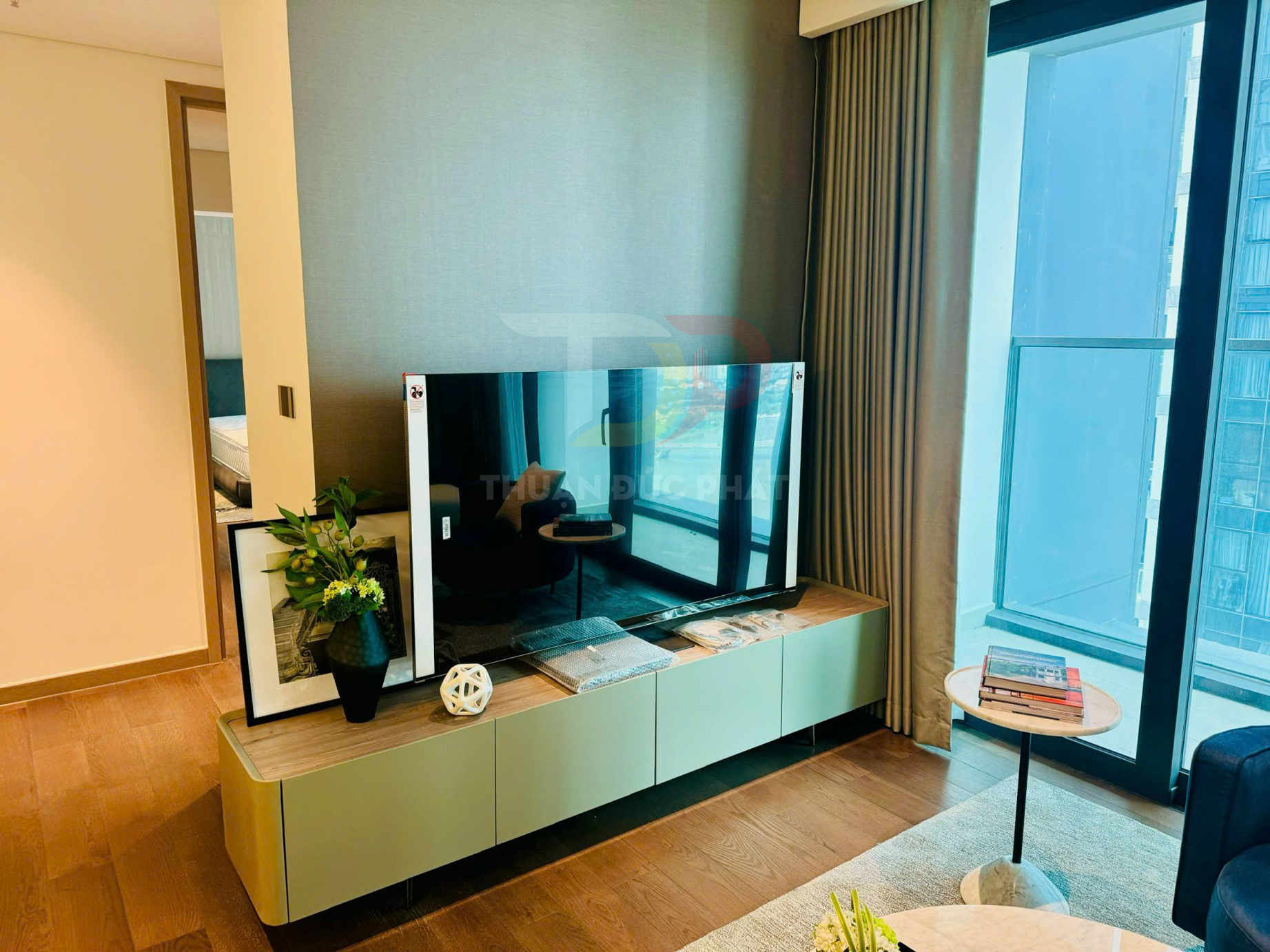 Tivi màn hình phẳng đặt trên kệ gỗ hiện đại trong phòng khách căn hộ sáng sủa có cửa kính lớn