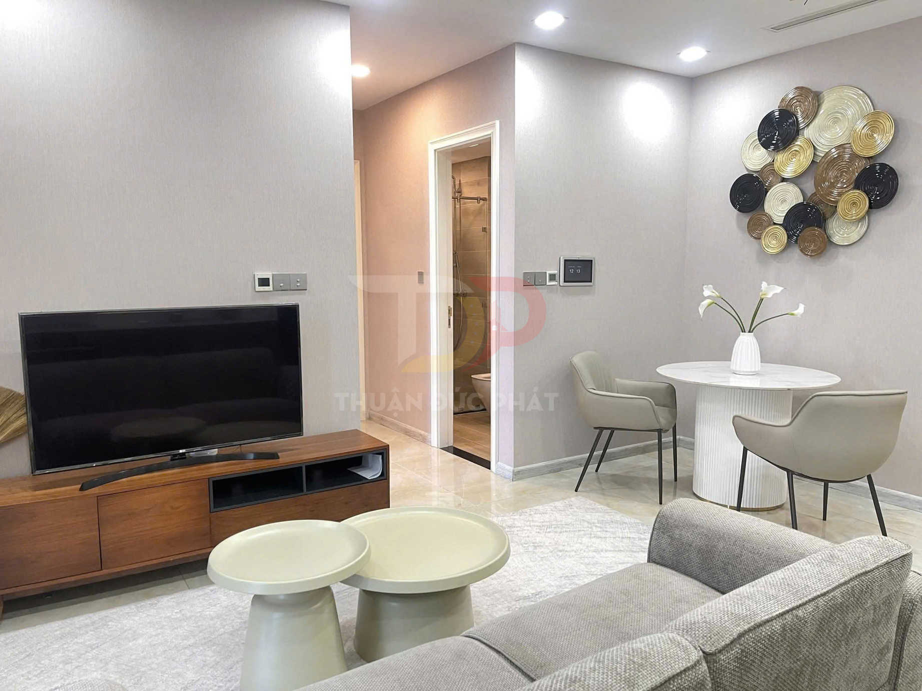 Phòng khách chung cư hiện đại với tivi màn hình phẳng, kệ gỗ, bàn trà đôi và bộ bàn ăn tròn hai ghế màu be