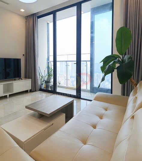 Sofa da màu kem trong phòng khách hiện đại với bàn trà gỗ và cửa kính lớn nhìn ra ban công