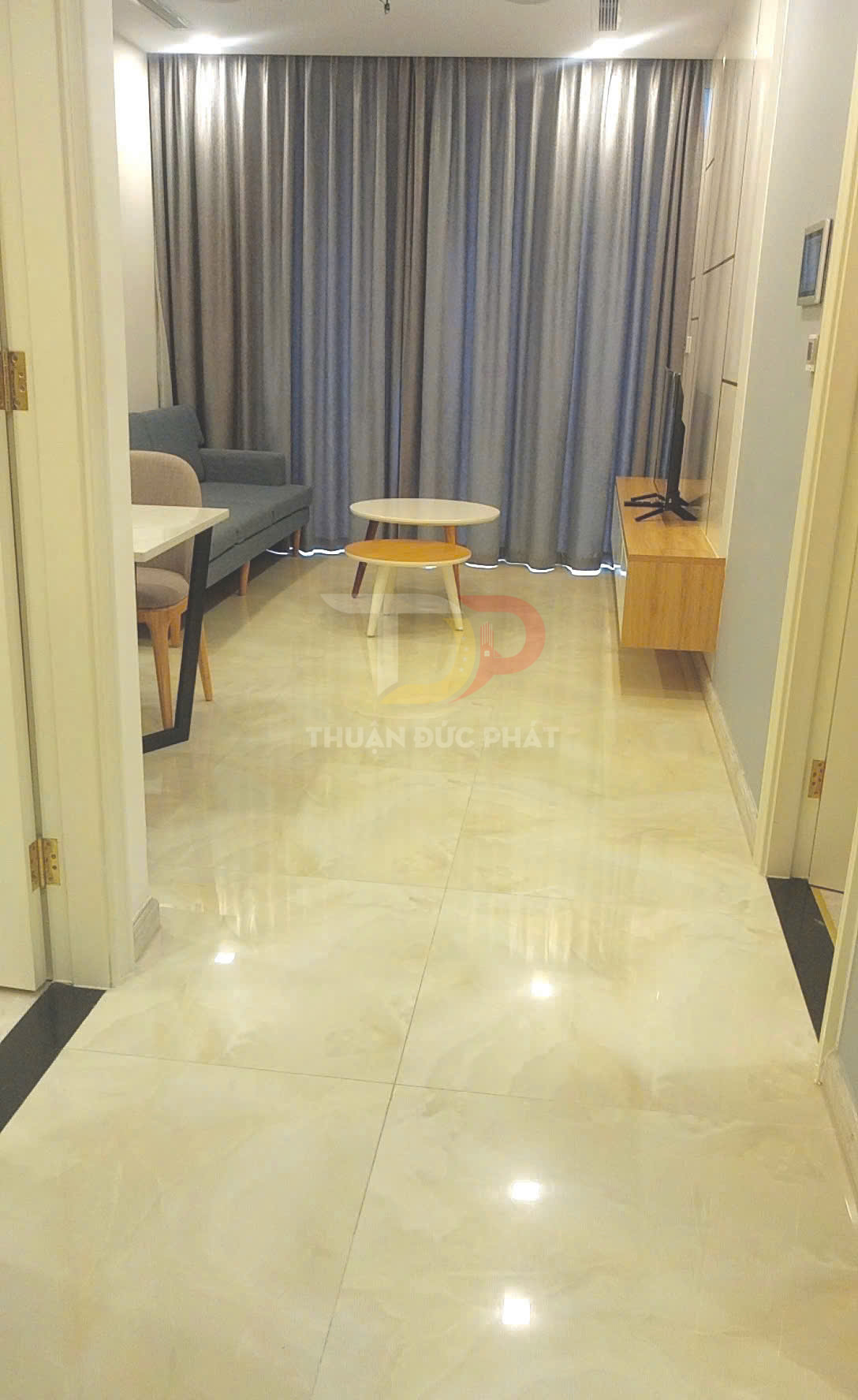 Sàn gạch bóng kiếng màu kem trong phòng khách chung cư hiện đại với sofa, bàn trà và kệ tivi gỗ