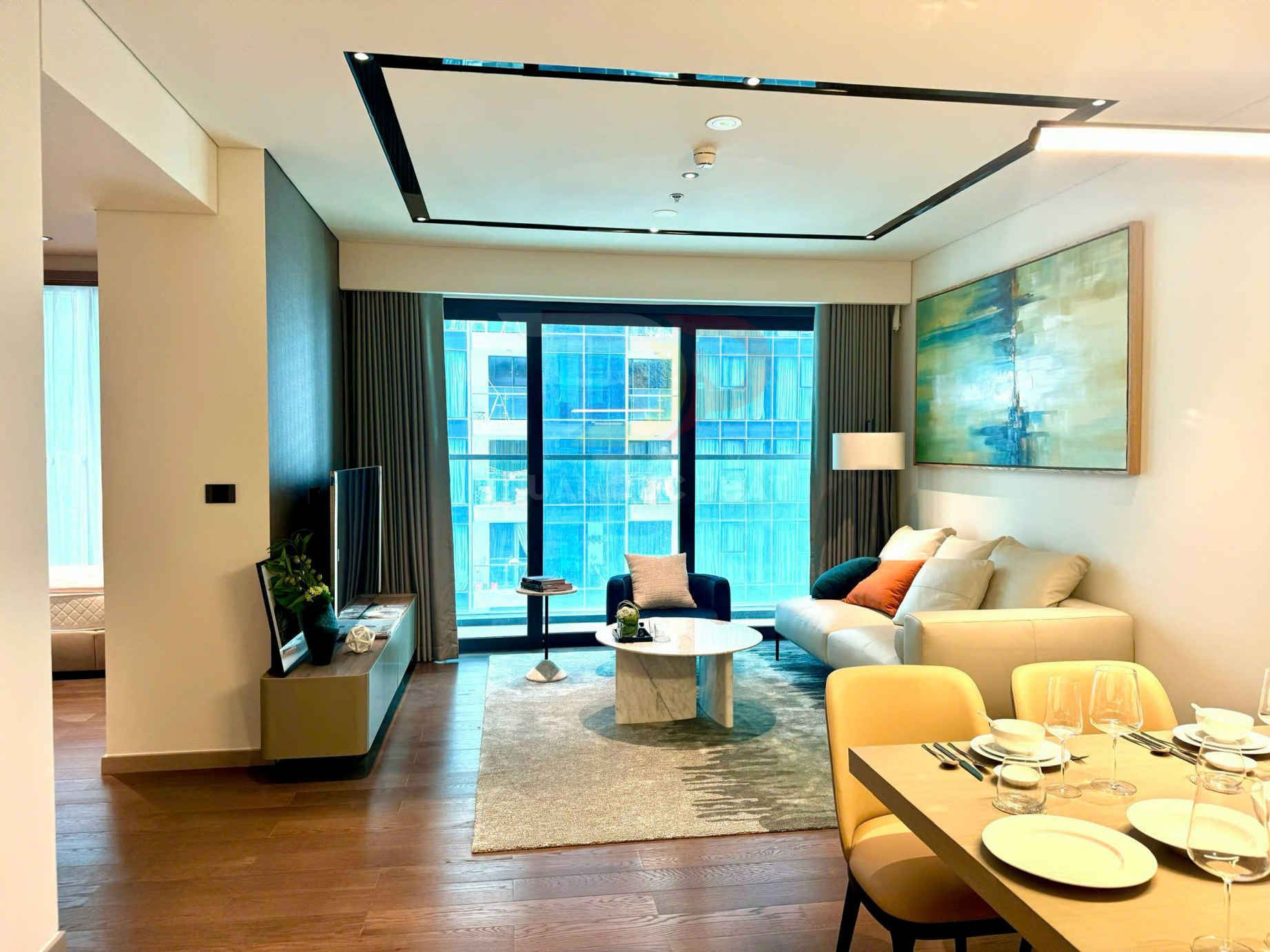 Phòng khách căn hộ hiện đại với sofa trắng, bàn trà đá, cửa kính lớn và bàn ăn bày sẵn bát đĩa