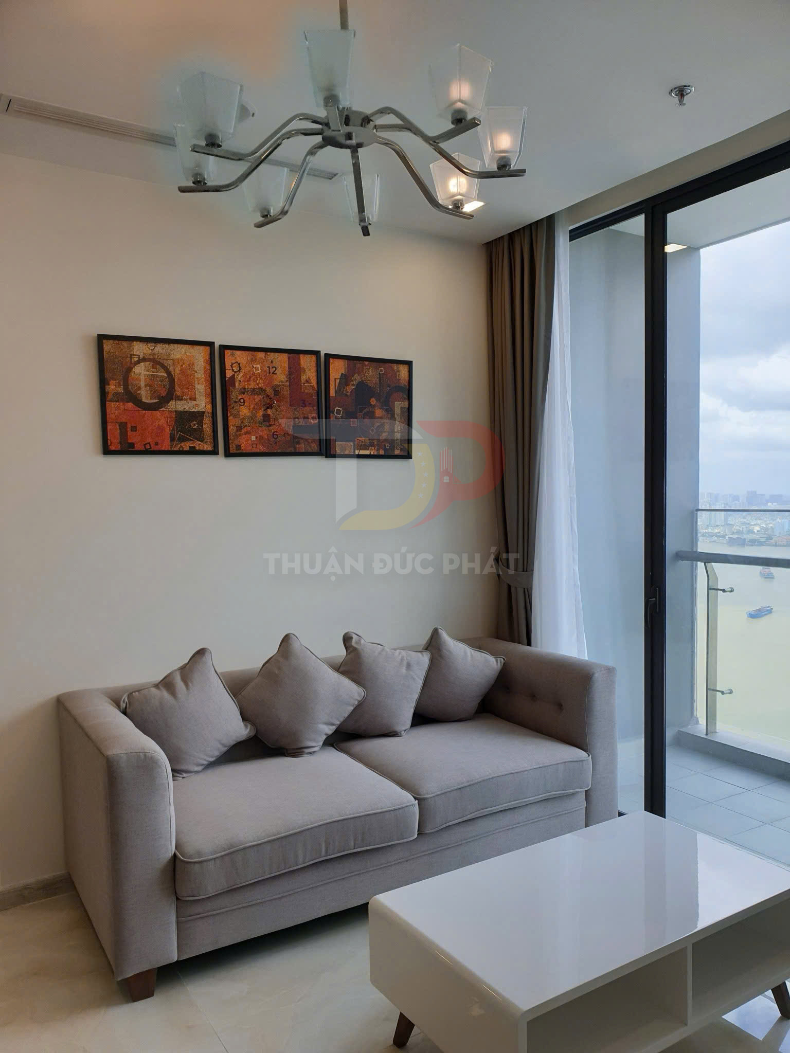 Sofa vải màu xám với bàn trà trắng trong phòng khách chung cư có cửa kính lớn nhìn ra ban công
