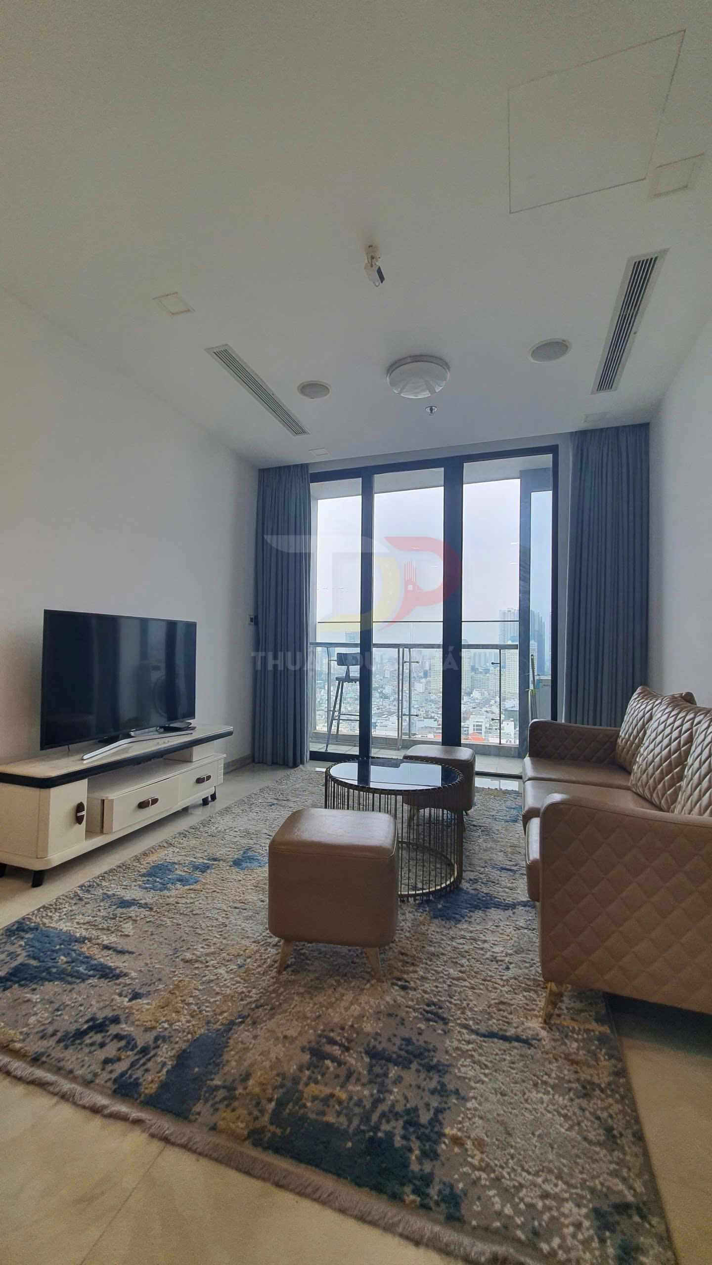 Phòng khách chung cư hiện đại với sofa da, bàn trà tròn, tivi màn hình phẳng và cửa kính lớn nhìn ra ban công