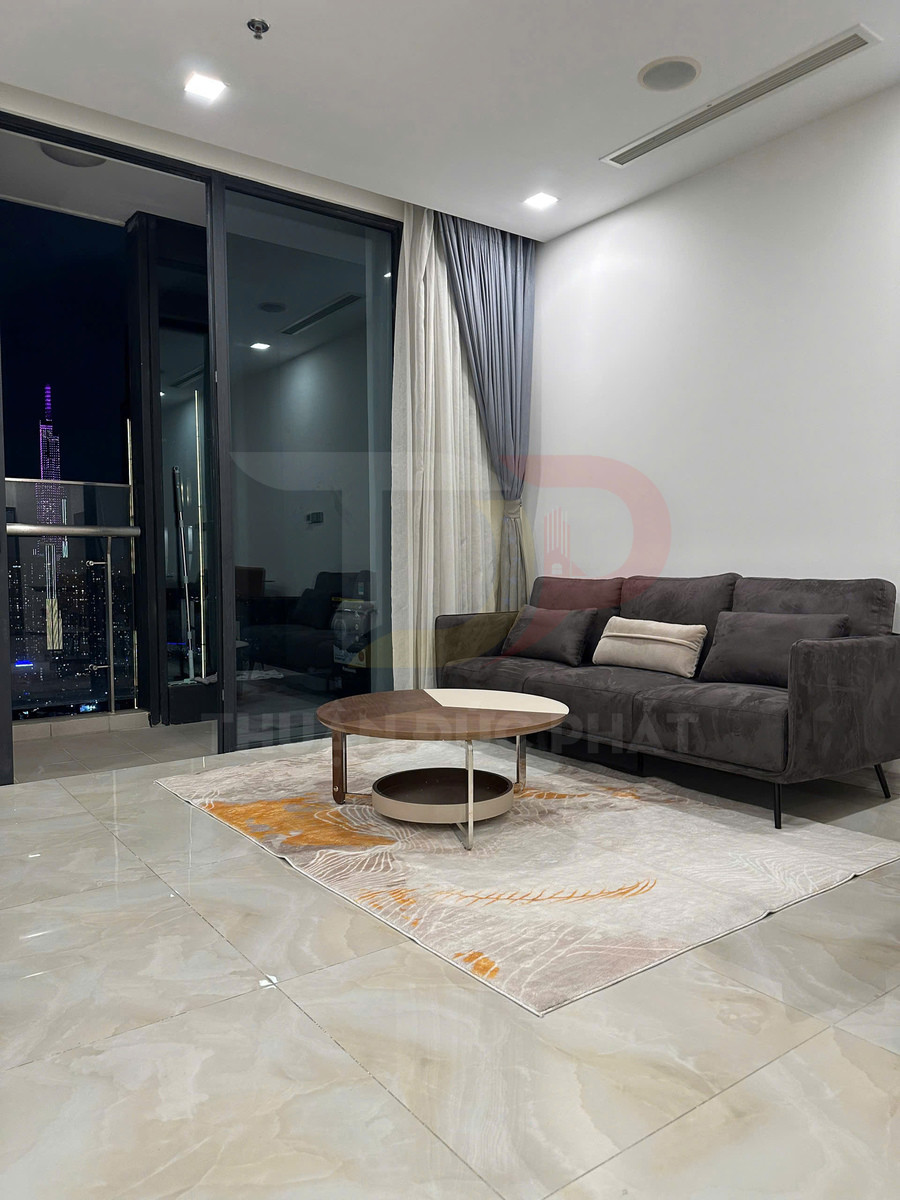 Phòng khách hiện đại với sofa xám, bàn trà tròn gỗ trên thảm trang trí cạnh cửa kính nhìn ra thành phố ban đêm