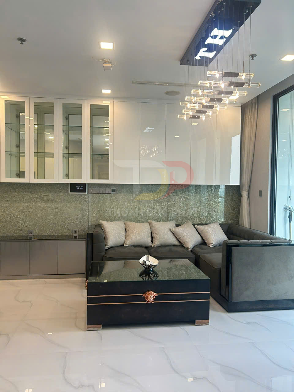 Sofa góc bọc nỉ màu xám với bàn trà mặt kính đen và đèn trần hiện đại trong phòng khách sang trọng