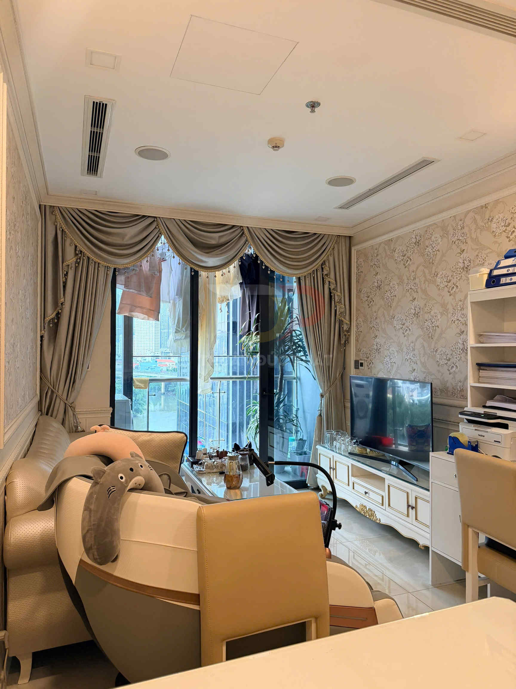 Phòng khách chung cư với sofa da, ghế massage, tivi màn hình phẳng và rèm cửa lớn nhìn ra ban công