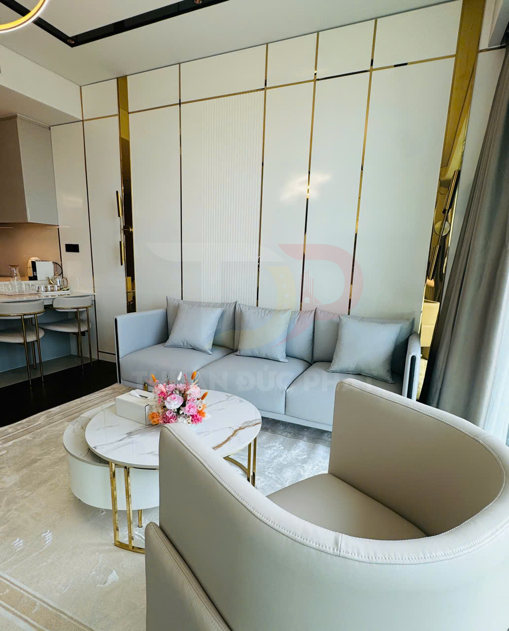 Phòng khách hiện đại với sofa xám, ghế bành, bàn trà mặt đá tròn và bình hoa trang trí