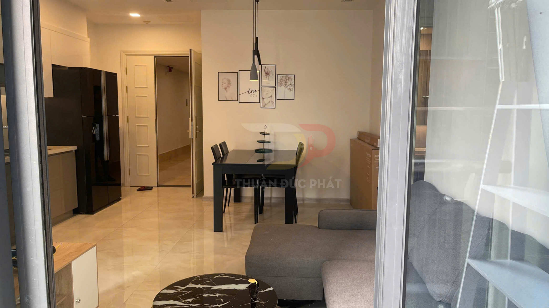 Phòng khách căn hộ với sofa xám, bàn trà đá đen và bàn ăn gỗ đen cạnh bếp hiện đại