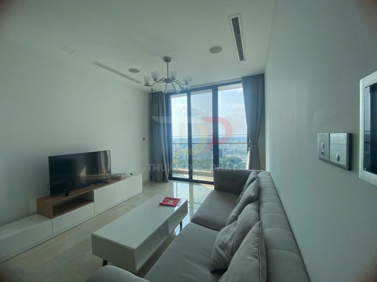 Phòng khách căn hộ hiện đại với sofa xám, bàn trà trắng, tivi màn hình phẳng và cửa kính lớn nhìn ra ban công