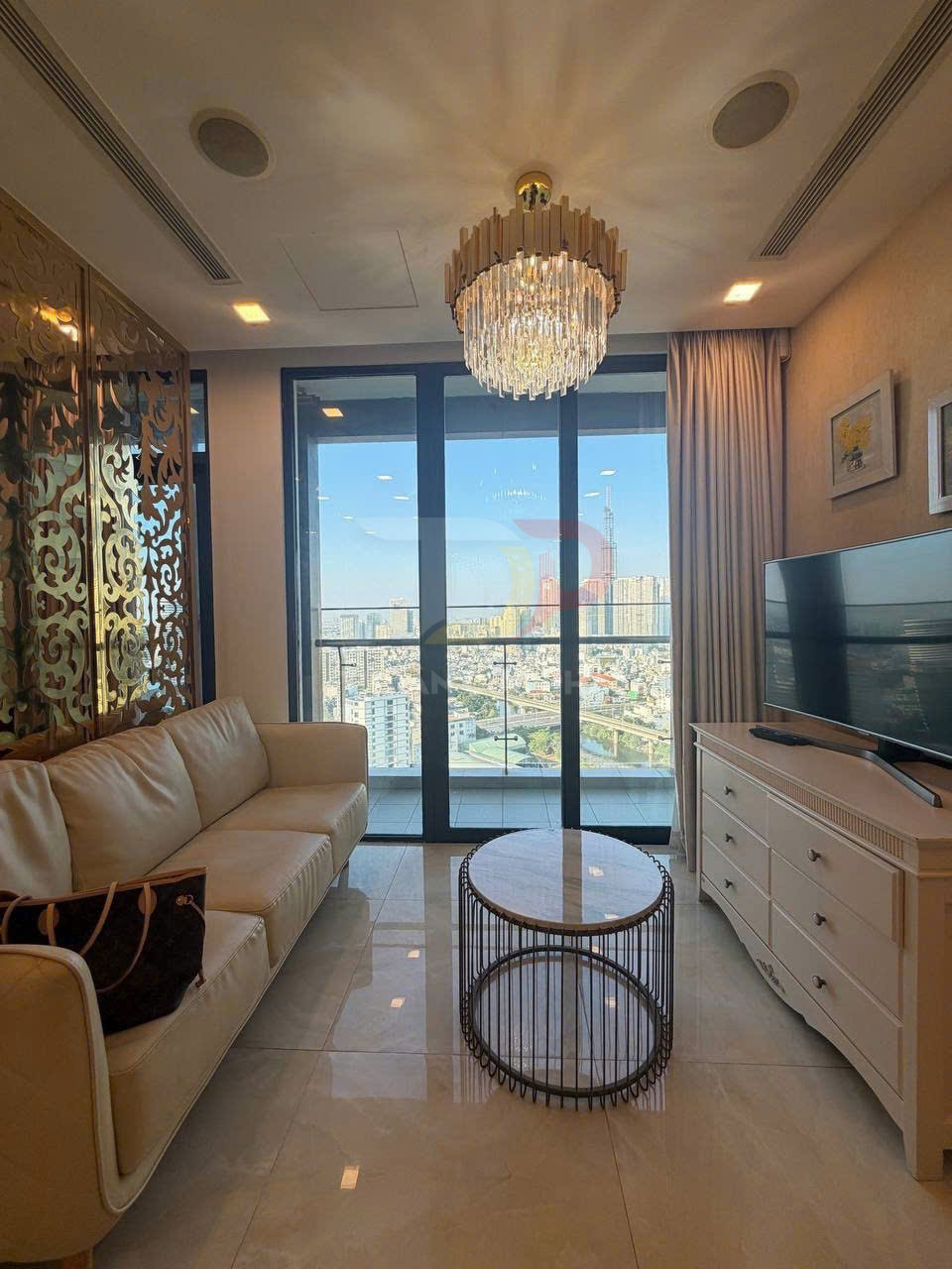 Phòng khách chung cư hiện đại với sofa da, bàn trà tròn, đèn chùm pha lê và cửa kính lớn nhìn ra thành phố