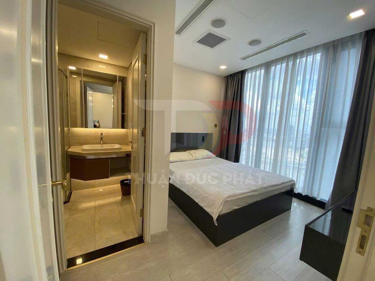 Phòng ngủ chung cư hiện đại với giường đôi cạnh cửa sổ lớn và nhà vệ sinh khép kín bên cạnh