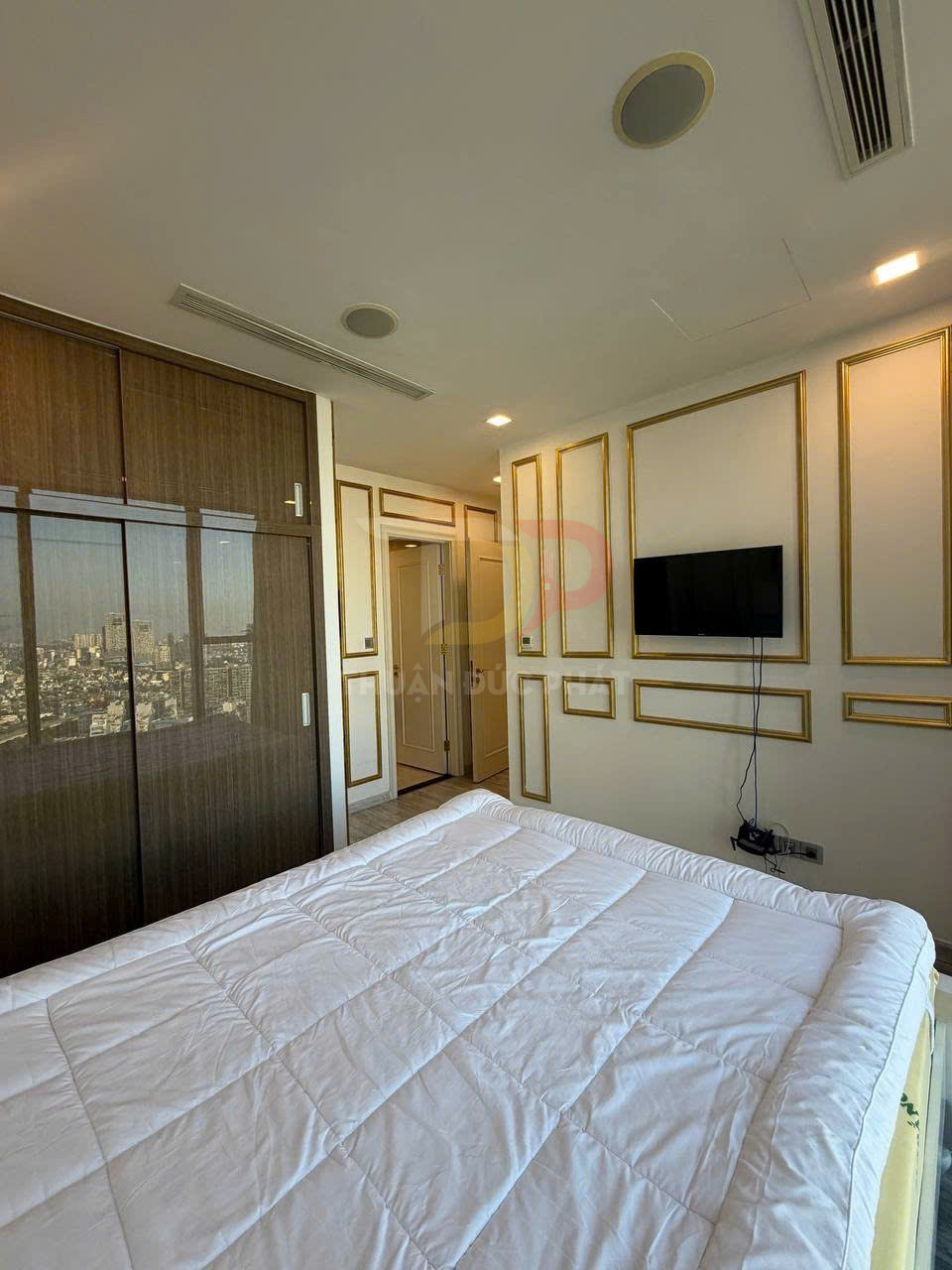 Chăn bông trắng trải trên giường trong phòng ngủ hiện đại có tủ gỗ và tivi treo tường