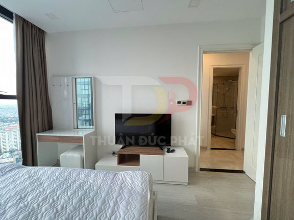 Phòng ngủ chung cư hiện đại với giường nệm, bàn trang điểm, tivi đặt trên kệ và cửa vào phòng tắm