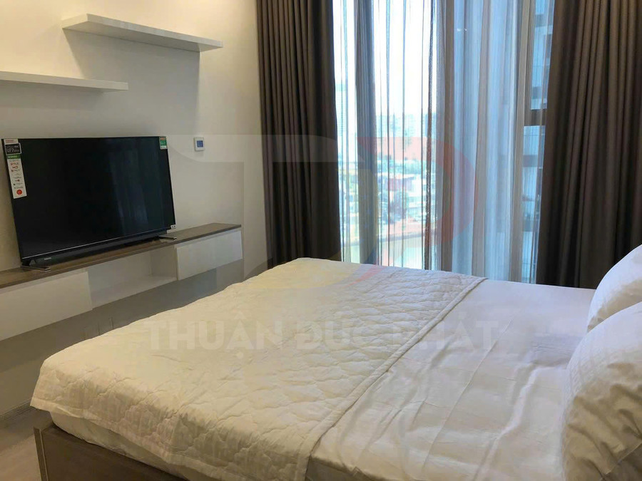 Phòng ngủ chung cư hiện đại với giường đôi trải ga trắng và tivi màn hình phẳng đặt trên kệ treo tường