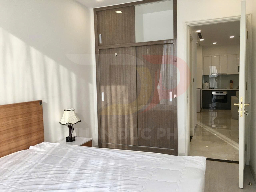 Phòng ngủ căn hộ với giường đôi, tủ quần áo cửa lùa gỗ và lối đi thông sang bếp hiện đại