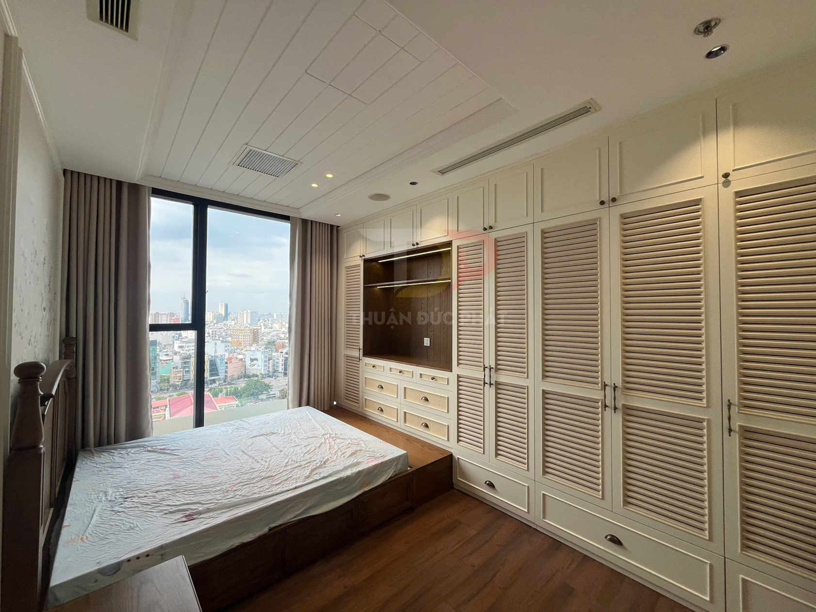 Tủ quần áo gỗ âm tường cánh lá sách màu kem trong phòng ngủ hiện đại có cửa sổ lớn nhìn ra thành phố