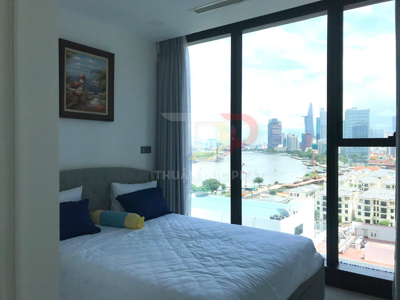 Phòng ngủ căn hộ với giường đôi cạnh cửa sổ kính lớn nhìn ra sông và khu đô thị hiện đại