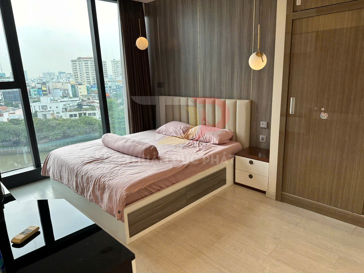 Giường ngủ gỗ hiện đại với ga gối màu hồng cạnh cửa sổ kính lớn view thành phố