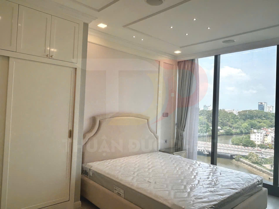 Phòng ngủ hiện đại với giường nệm mới cạnh tủ quần áo và cửa kính lớn nhìn ra sông