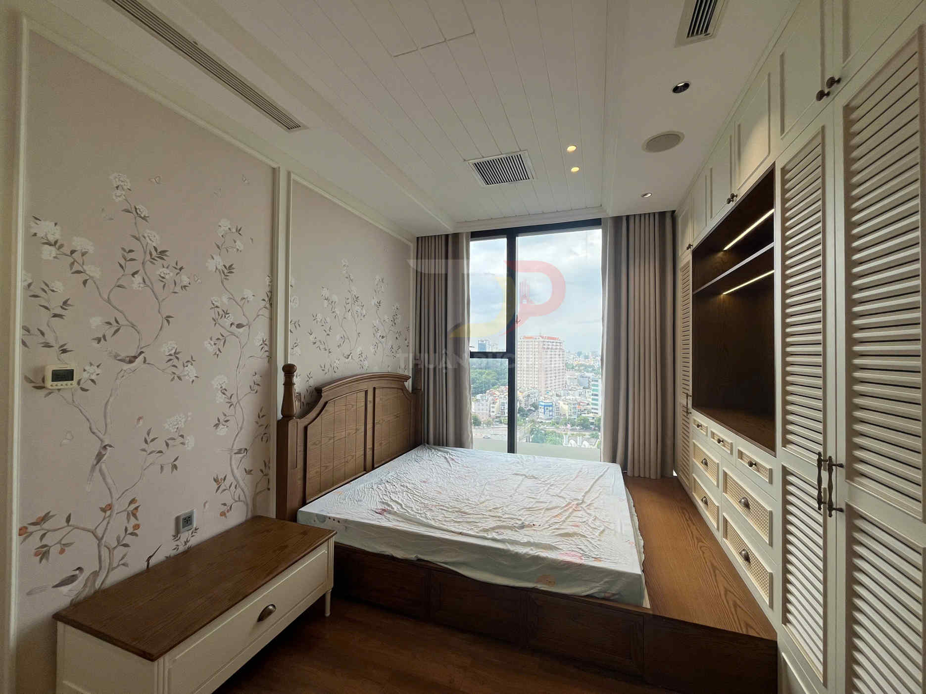 Phòng ngủ chung cư với giường gỗ, tủ quần áo âm tường và cửa sổ lớn nhìn ra thành phố