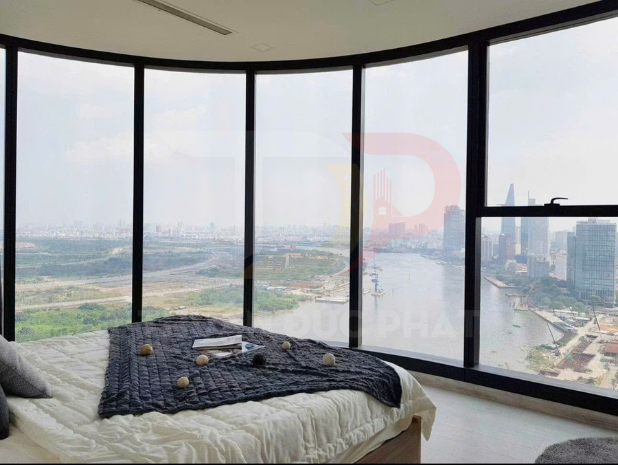Phòng ngủ căn hộ cao cấp với giường cạnh cửa kính lớn nhìn ra sông và toàn cảnh thành phố