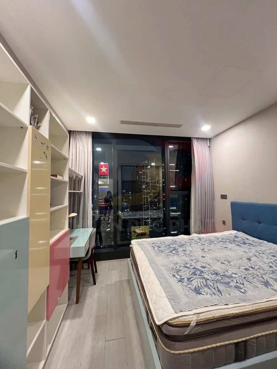 Phòng ngủ hiện đại với giường nệm lớn, ga họa tiết hoa và bàn học cạnh cửa kính nhìn ra thành phố