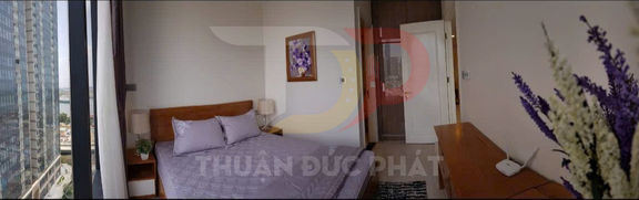 Phòng ngủ chung cư với giường đôi chăn ga gối màu tím cạnh cửa sổ lớn view thành phố