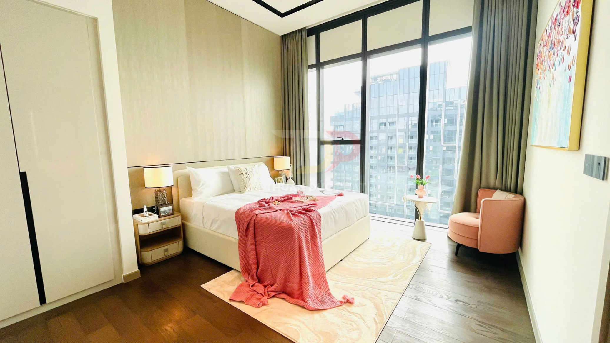 Phòng ngủ chung cư hiện đại với giường đôi trắng, chăn hồng, cửa sổ kính lớn và ghế bành hồng cạnh bàn nhỏ