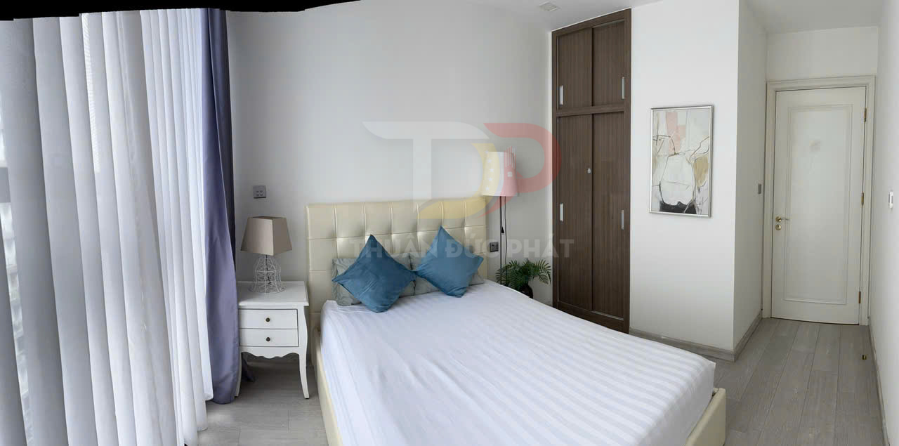 Phòng ngủ hiện đại với giường đôi bọc da trắng, gối xanh, tủ quần áo gỗ và rèm cửa lớn sáng màu