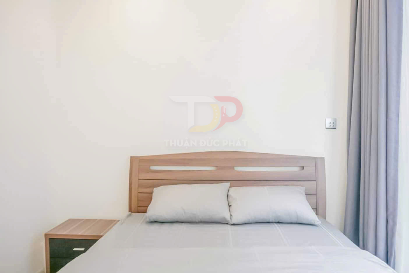 Giường ngủ gỗ hiện đại với nệm và gối màu xám nhạt cạnh tủ đầu giường nhỏ