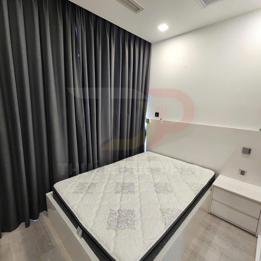Nệm ngủ màu trắng hoa văn xám đặt trên giường gỗ cạnh rèm cửa tối màu trong phòng ngủ hiện đại