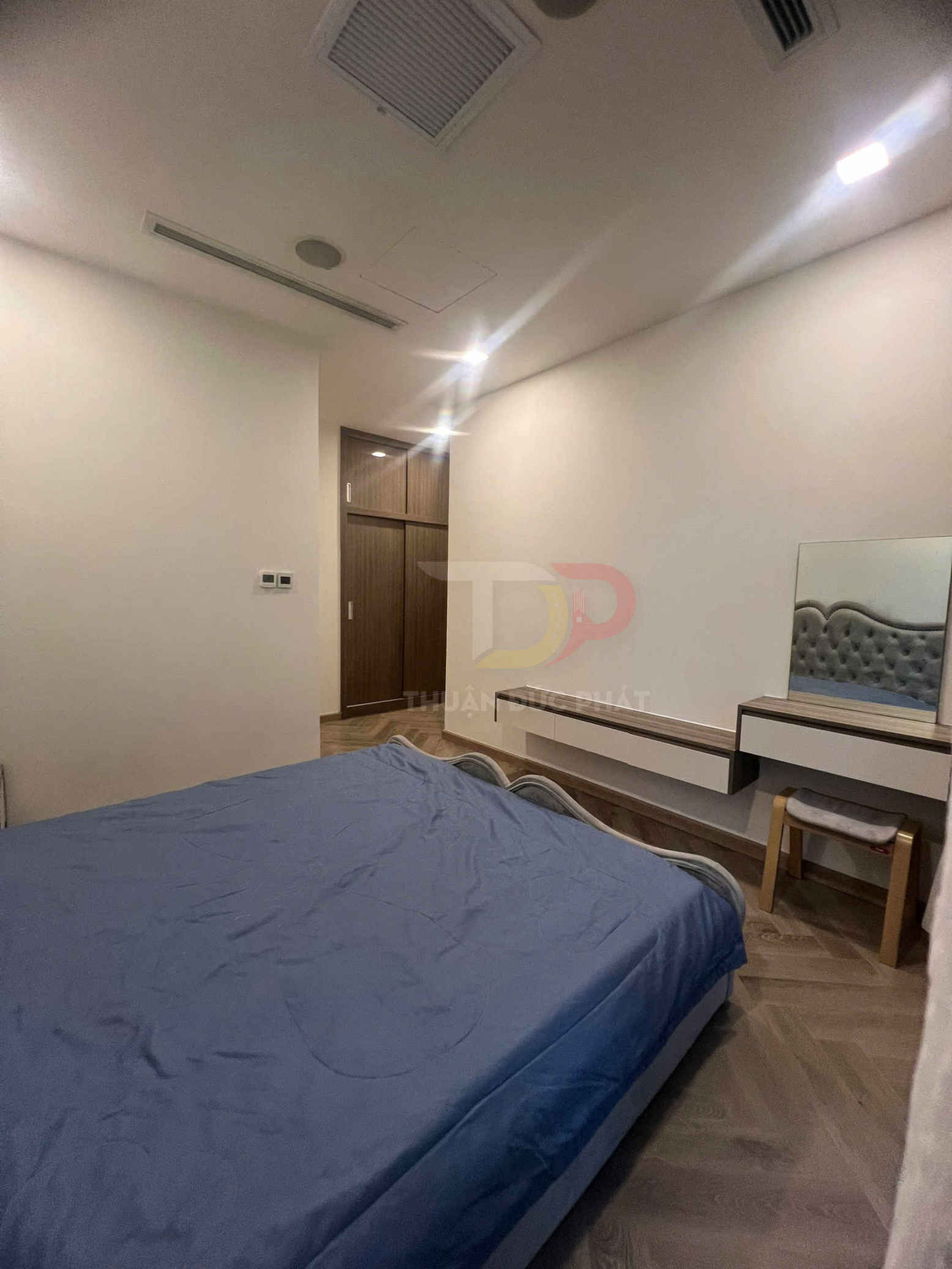 Phòng ngủ hiện đại với giường nệm bọc ga xanh, tủ quần áo gỗ và bàn trang điểm nhỏ có ghế đệm