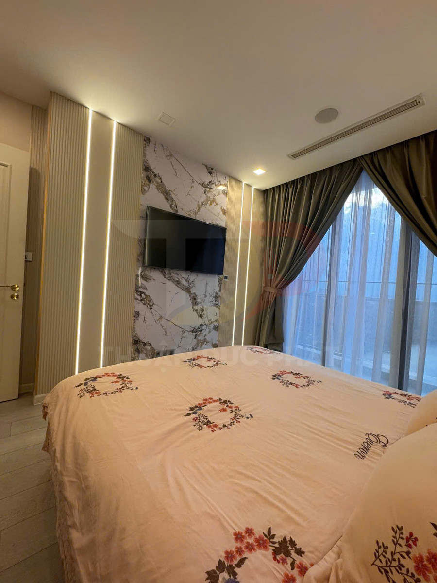 Phòng ngủ hiện đại với giường ga hoa màu be, tivi treo tường và rèm cửa lớn cạnh cửa sổ