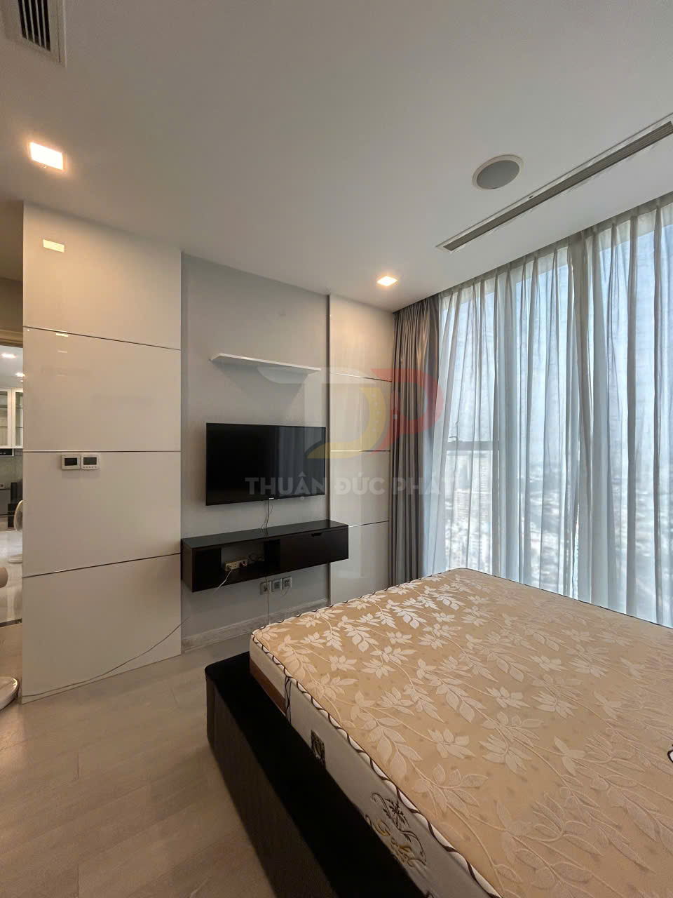 Phòng ngủ hiện đại với giường nệm hoa văn, tivi treo tường và rèm cửa sổ lớn đón ánh sáng tự nhiên
