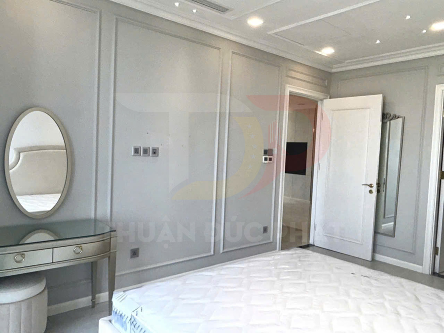 Phòng ngủ hiện đại với giường nệm trắng, bàn trang điểm gương oval và tường ốp phào chỉ màu xám nhạt