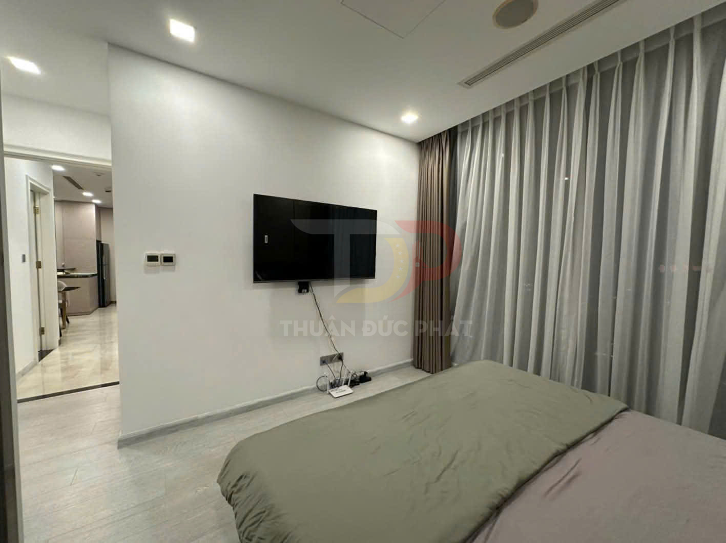 Phòng ngủ hiện đại với tivi treo tường đối diện giường và rèm cửa sổ hai lớp màu sáng