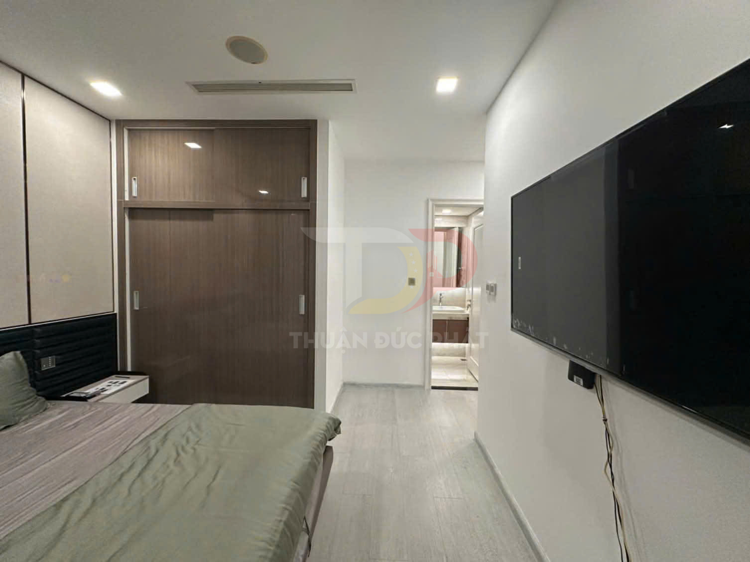 Phòng ngủ hiện đại với tủ quần áo gỗ cửa lùa, giường bọc nệm và tivi treo tường đối diện lối vào nhà tắm