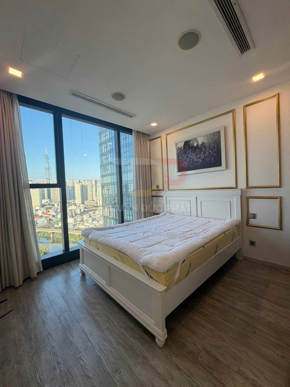 Phòng ngủ chung cư với giường ngủ gỗ trắng, nệm dày và cửa kính lớn nhìn ra thành phố