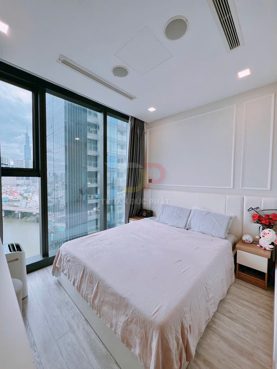 Phòng ngủ chung cư hiện đại với giường đôi cạnh cửa kính lớn view sông và tòa nhà cao tầng