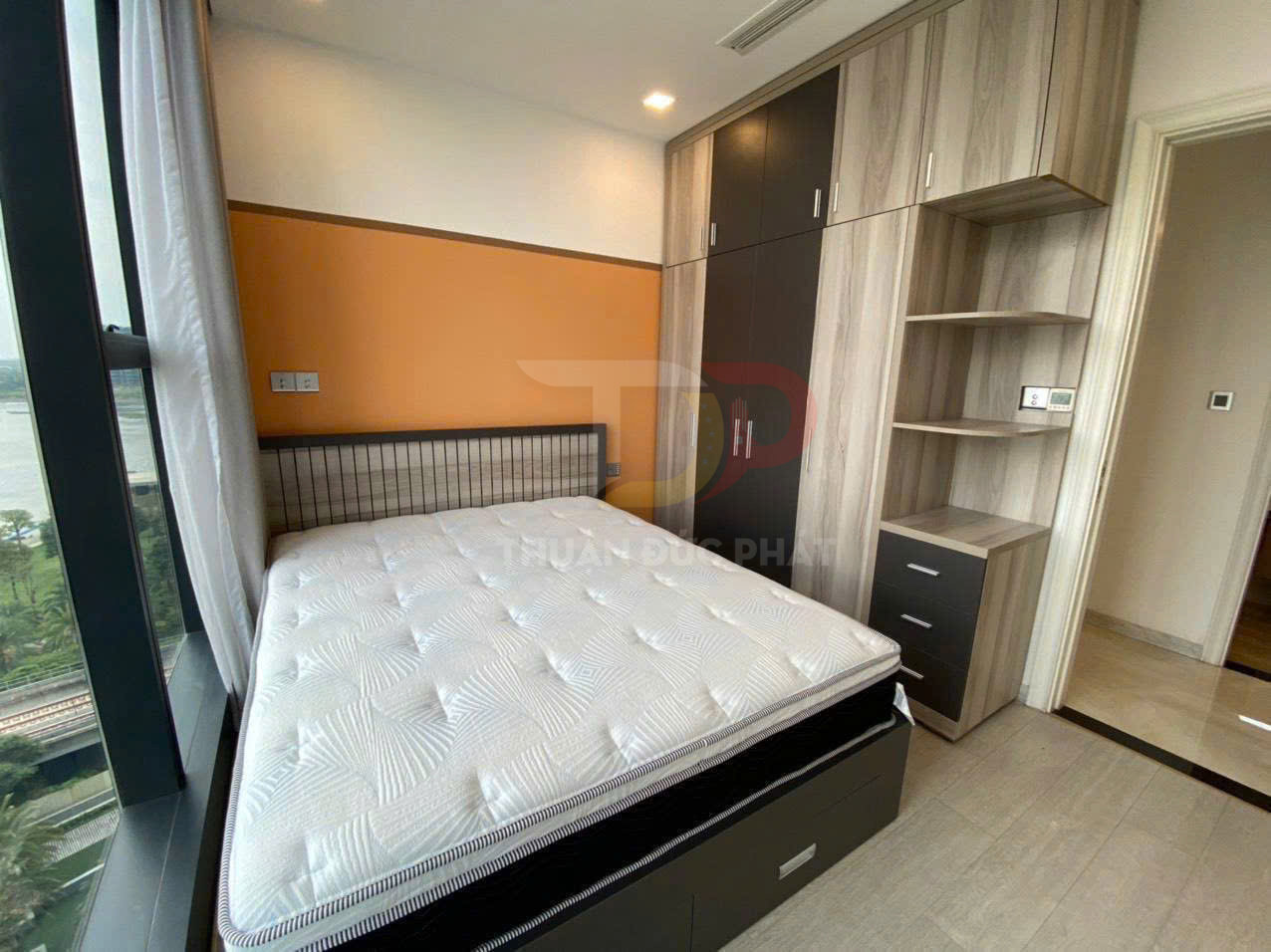 Giường ngủ gỗ có nệm trắng cạnh tủ quần áo âm tường trong phòng ngủ sáng cửa sổ lớn