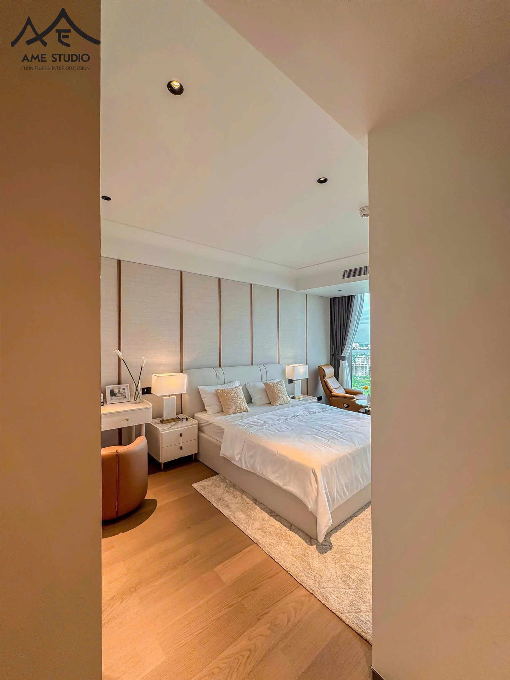 Phòng ngủ hiện đại với giường đôi bọc nệm, táp đầu giường và ghế thư giãn cạnh cửa sổ lớn