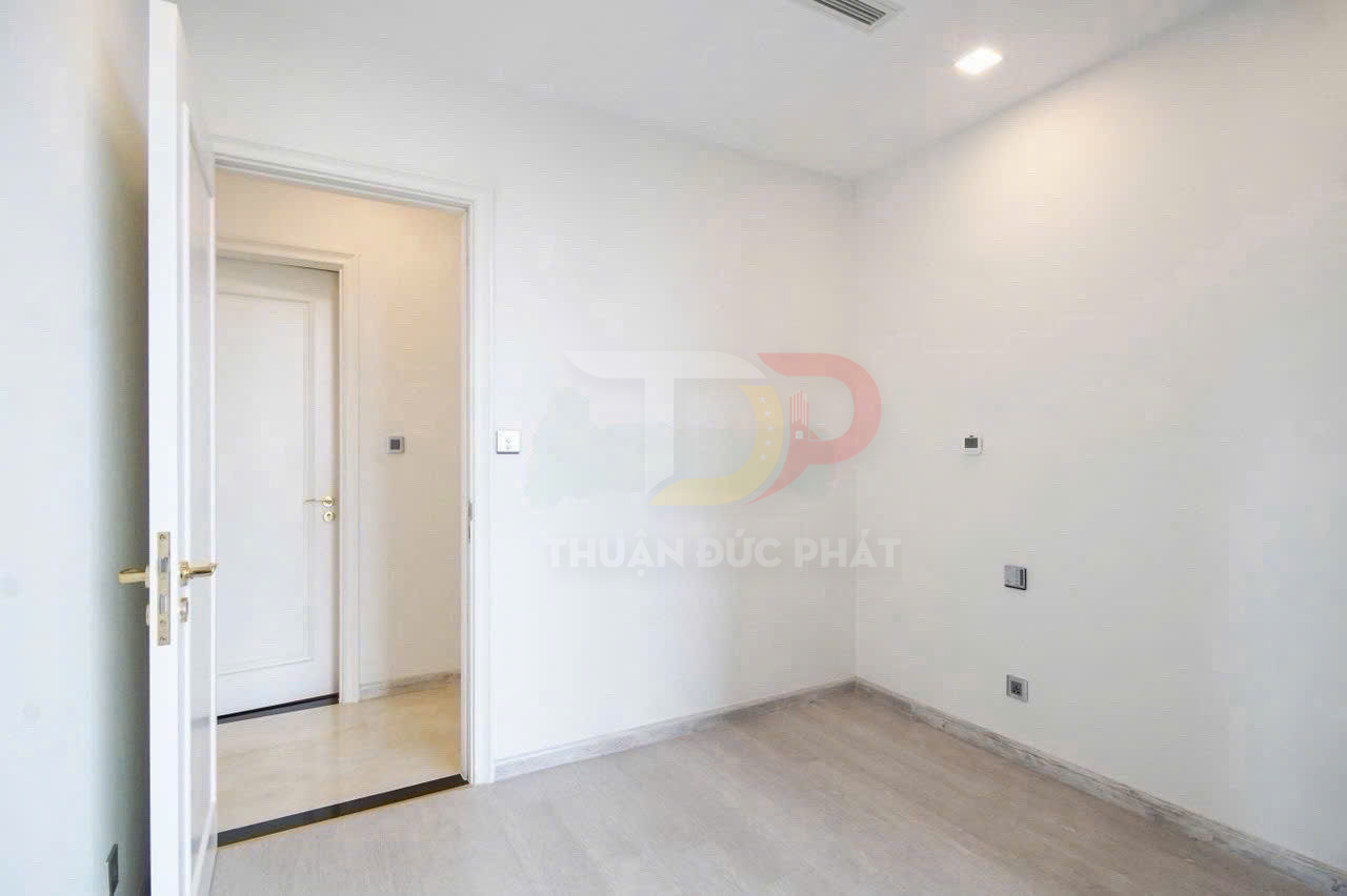 Phòng trống sơn trắng với cửa gỗ mở, sàn gỗ sáng màu và ổ cắm điện âm tường