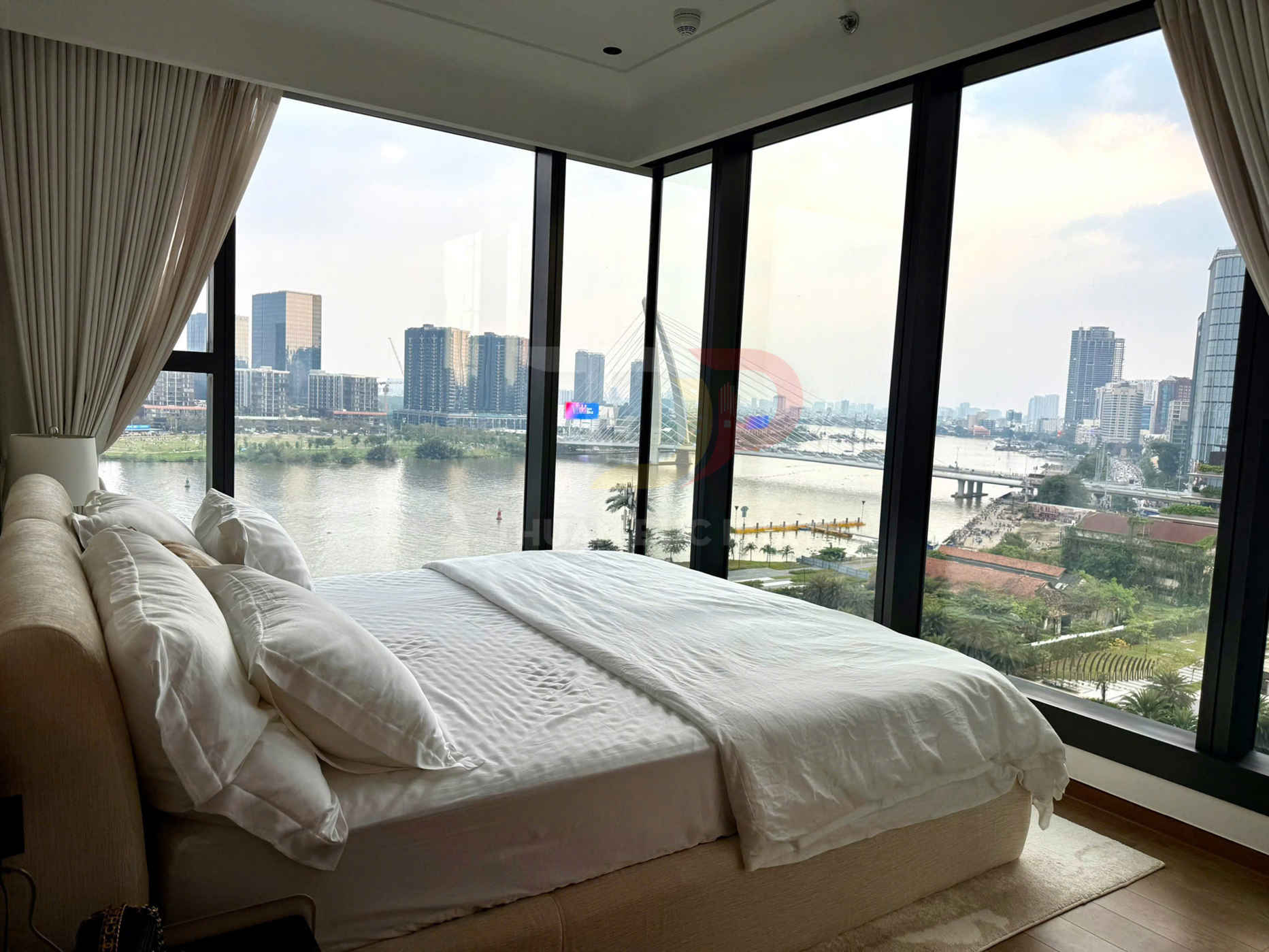 Phòng ngủ giường đôi trắng cạnh cửa kính lớn nhìn ra sông và toàn cảnh thành phố