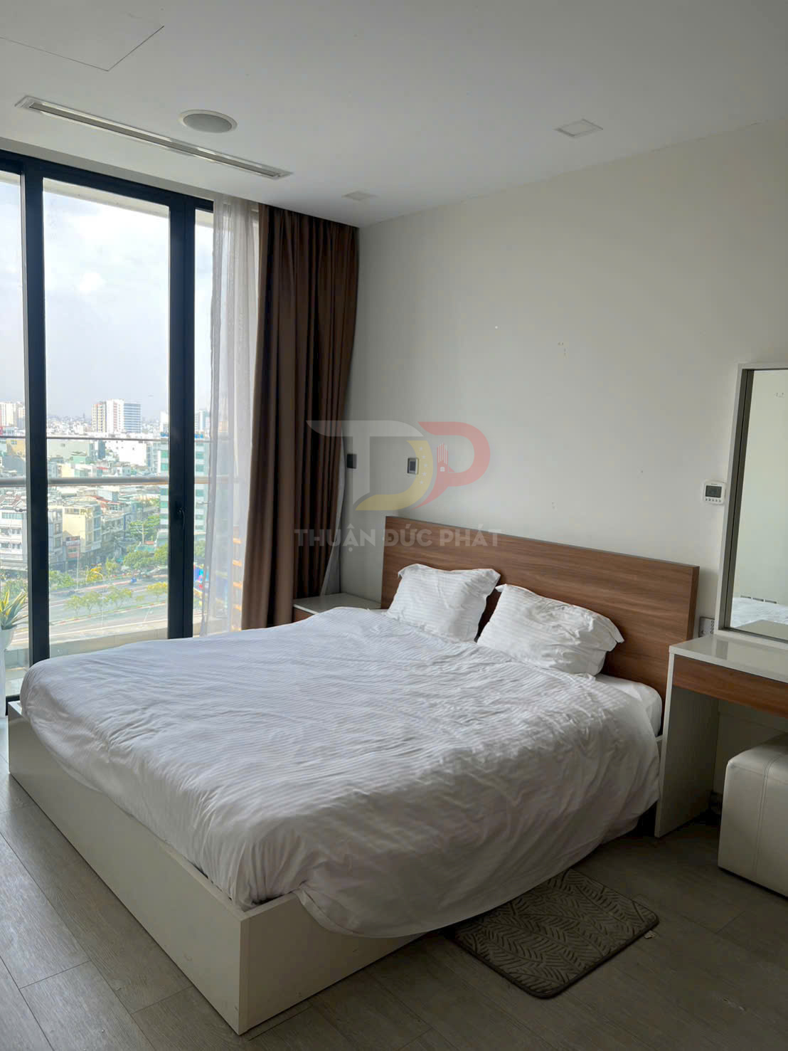 Giường ngủ đôi với ga trắng cạnh cửa kính lớn nhìn ra thành phố, nội thất hiện đại tối giản