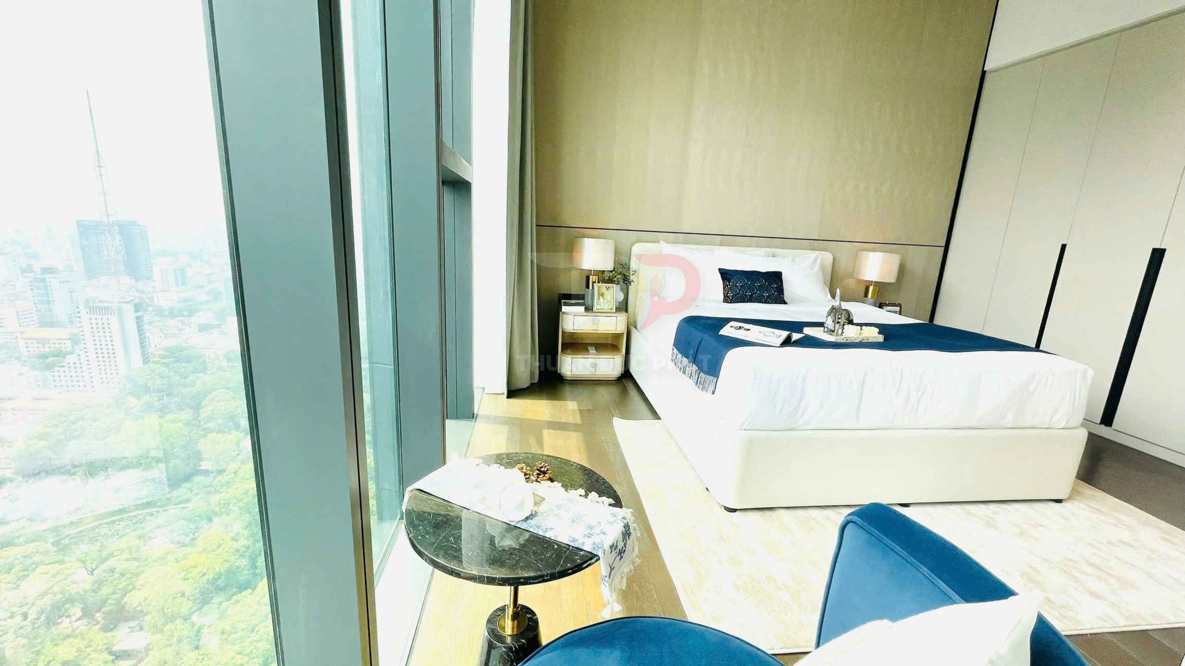 Phòng ngủ chung cư cao cấp với giường đôi trắng chăn xanh cạnh cửa kính lớn view thành phố