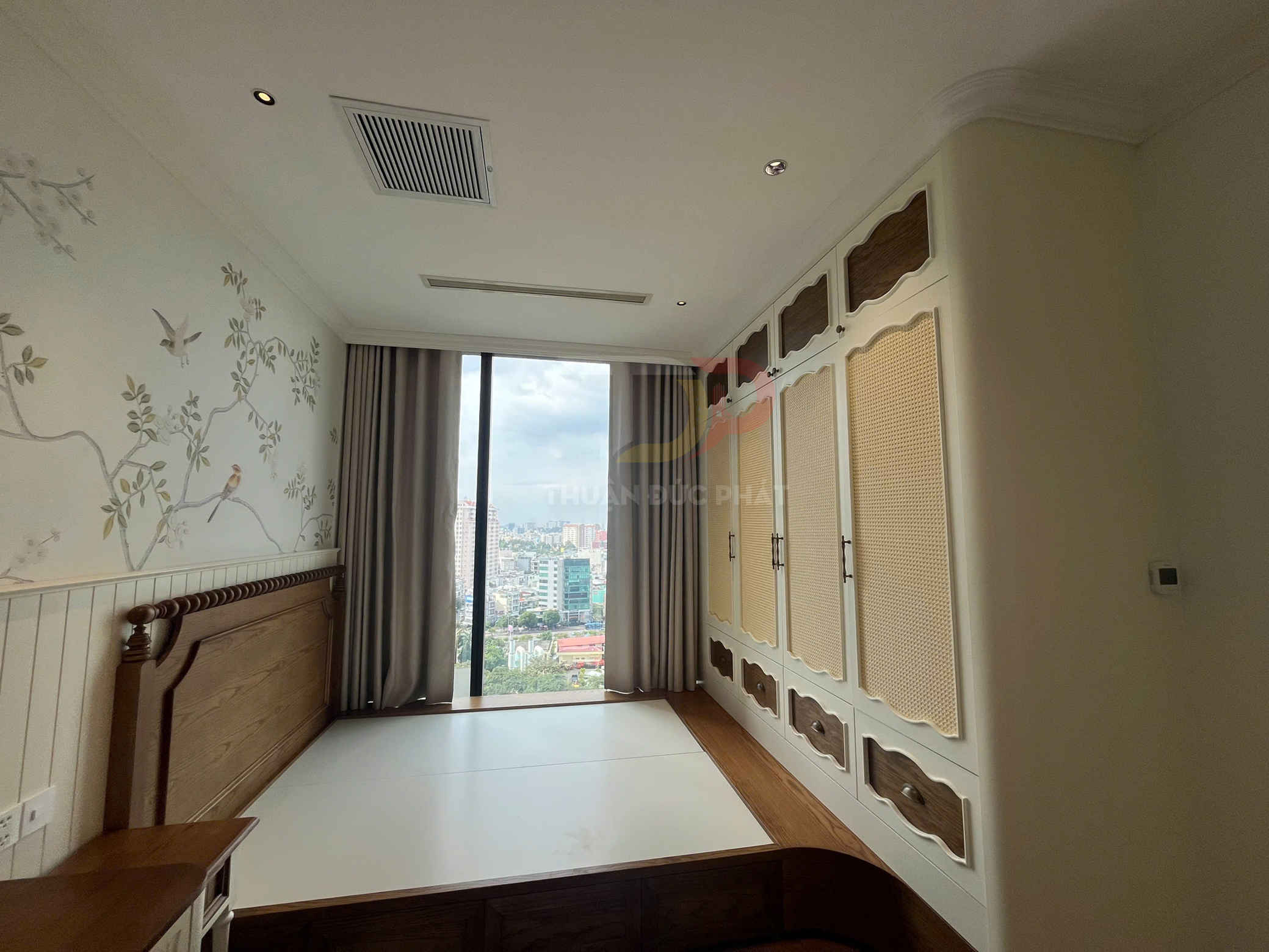 Phòng ngủ nhỏ với giường gỗ liền tủ quần áo âm tường và cửa sổ kính lớn nhìn ra thành phố