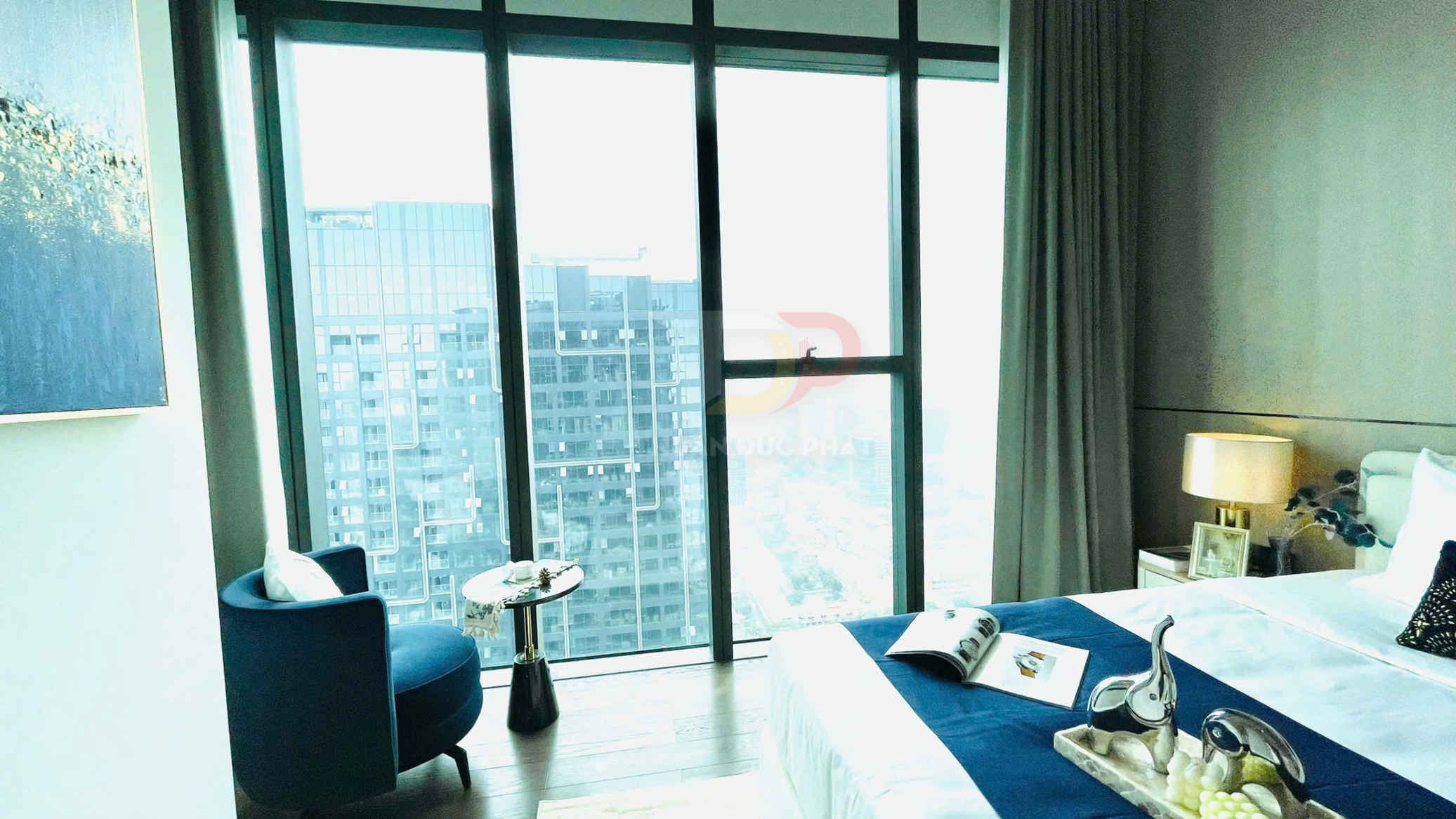 Phòng ngủ chung cư cao cấp với cửa kính lớn, giường trắng xanh và ghế sofa đơn cạnh bàn nhỏ