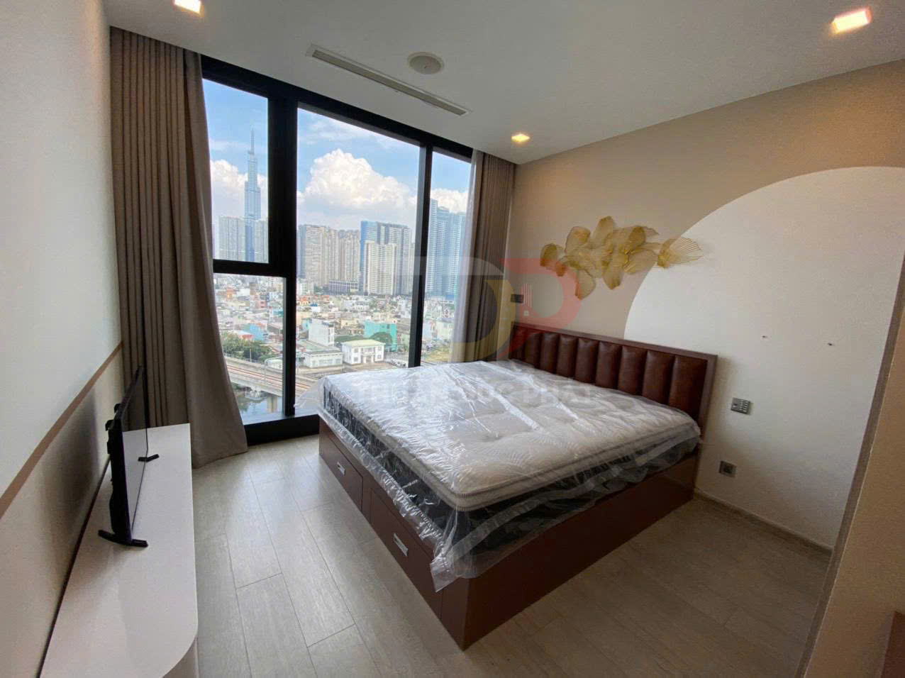 Phòng ngủ chung cư với giường nệm mới bọc nilon cạnh cửa sổ lớn nhìn ra thành phố